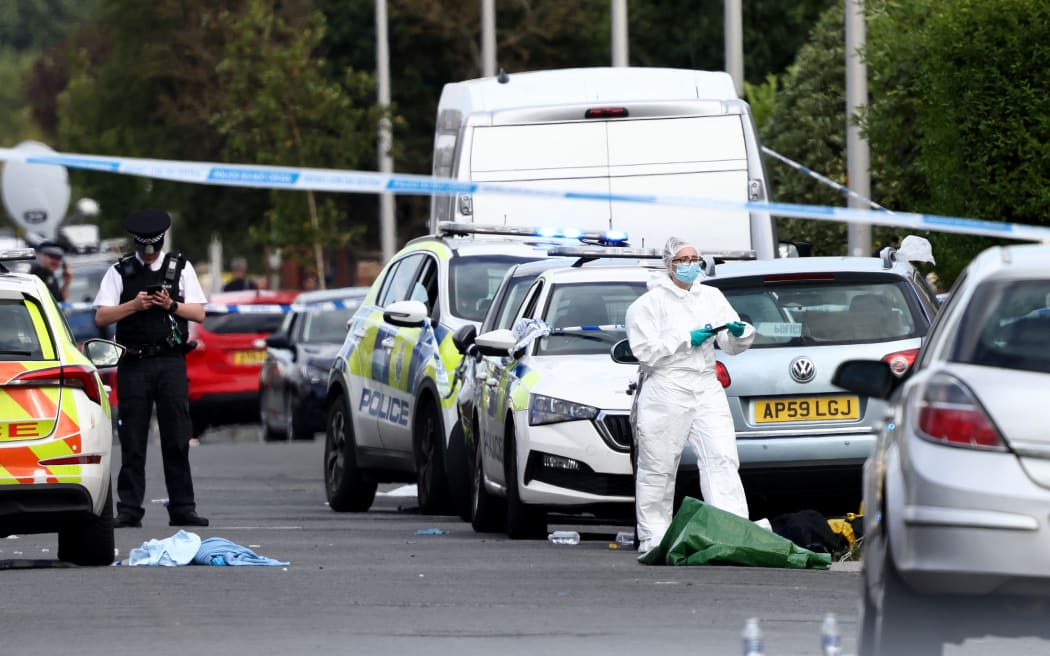 Police officers and forensic personnel stand behind a cordon on Hart Street in Southport, northwest England, on July 29, 2024, following a knife attack. A suspected knife attack in northern England left at least eight people injured, believed to include children, emergency services said. (Photo by Darren Staples / AFP)