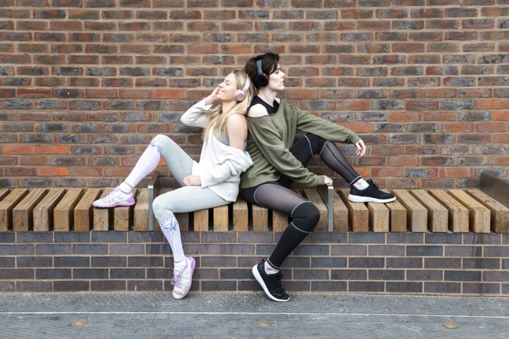 Friends relaxing, two girls listening to music on headphones on a street.