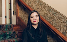 Cadence Chung sits on a staircase, next to a wall with decorative wallpaper in the lower part.