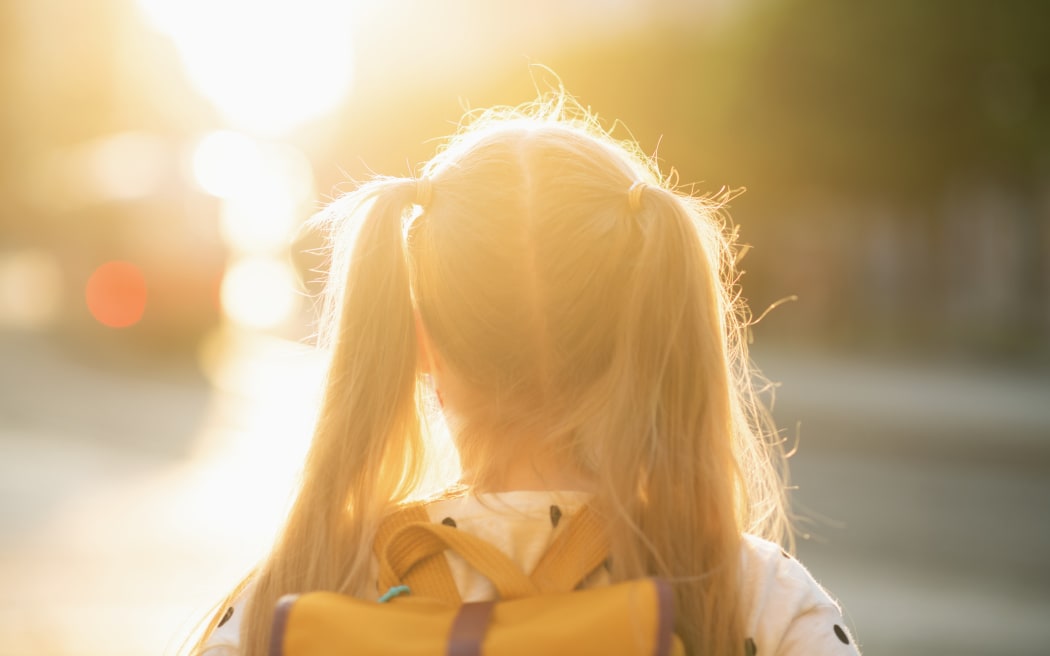 A schoolgirl with yellow backpack going to school outside.