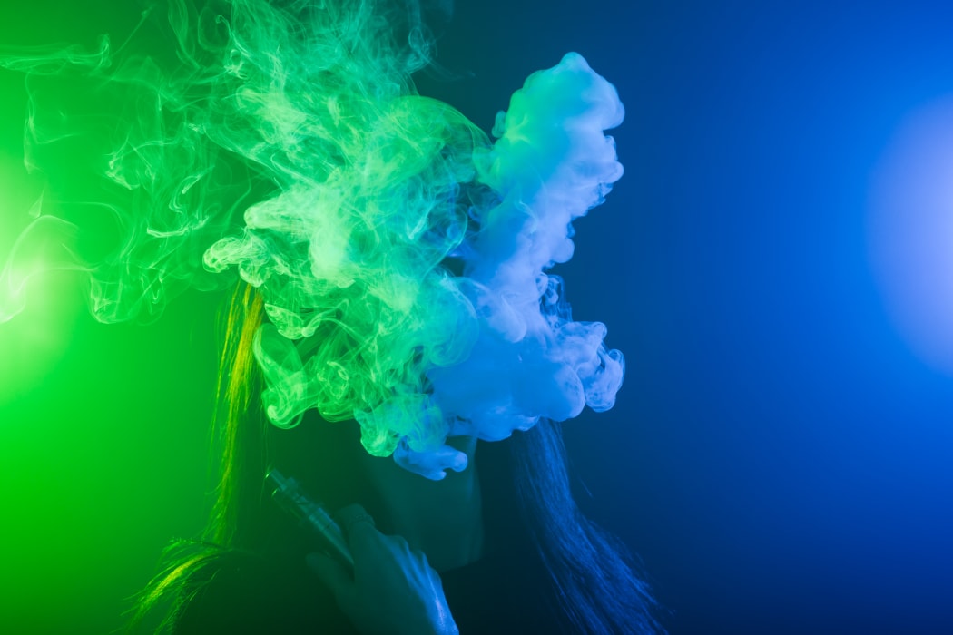 Portrait of asian woman smoking vape or e-cigarette in neon light at black background