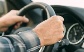 Man's hands holding the steering wheel, driving a car