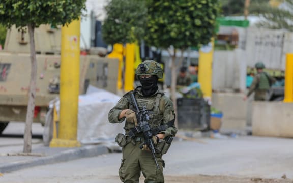 An Israeli soldier stands guard next to a barrier as the military closes Hebron's H2 southern sector in the occupied West Bank on January 19, 2026. Troops imposed a curfew on approximately 70,000 people while searching for weapons and wanted individuals, erecting new gates and earth mounds to isolate the area. Following the 1995 Oslo Agreement and 1997 Hebron Agreement, the city remains divided, with H2, including the Old City of Hebron, under Israeli military control while H1 is administered by the Palestinian Authority. Most Palestinians live in the H2 sector. (Photo by mosab shawer and Mosab Shawer / Middle East Images via AFP)