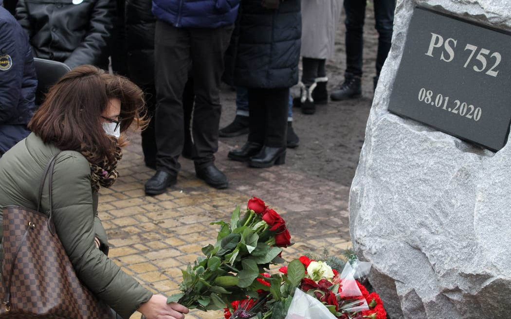 A woman lays flowers during an honoring ceremony in the memory of victims of crash flight 752 of the Ukraine International Airlines (UIA) in Iran, near a stone for a future memorial in a park which will a square in memory of the victims of flight PS752, in Kyiv, Ukraine on 8 January 2021.