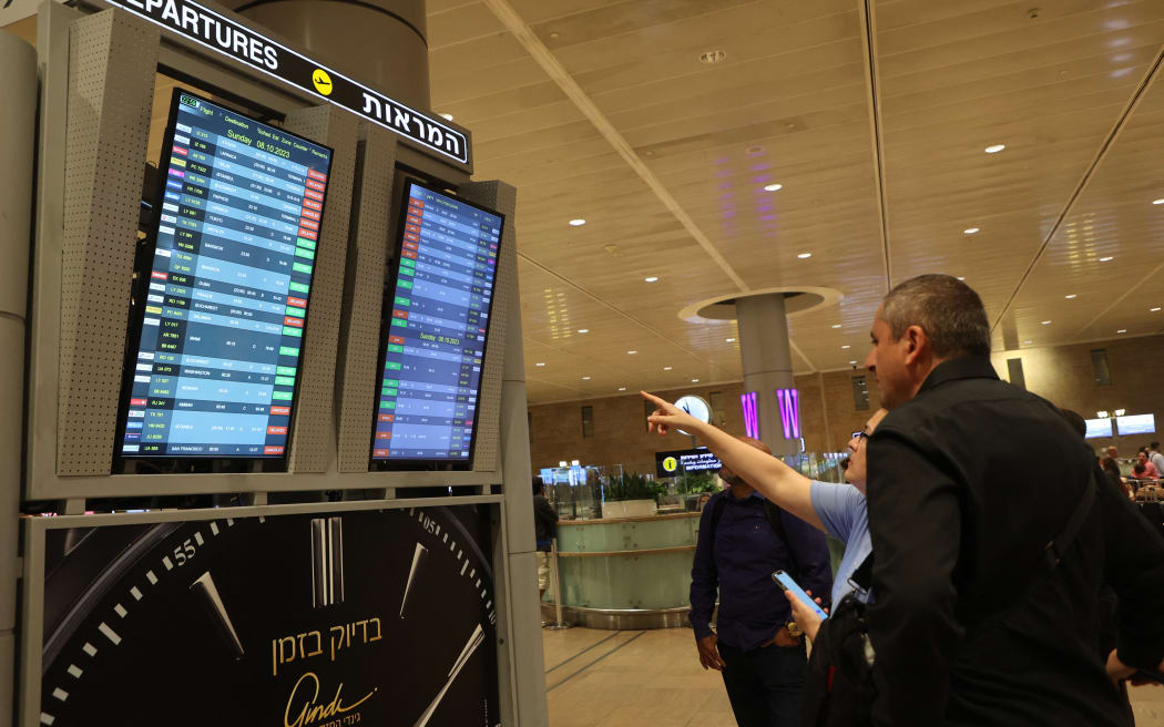 Passengers look at a departure board at Ben Gurion Airport near Tel Aviv, Israel, on October 7, 2023, as flights are canceled because of the Hamas surprise attacks. The conflict sparked major disruption at Tel Aviv airport, with American Airlines, Emirates, Lufthansa and Ryanair among carriers with cancelled flights.