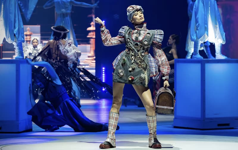 A woman in decorated short dress, socks and a hat strikes a robotic pose.