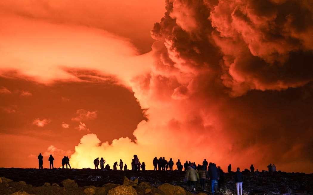 People gather to watch as molten lava flows out from a fissure on the Reykjanes peninsula north of the evacuated town of Grindavik, western Iceland on 16 March, 2024.