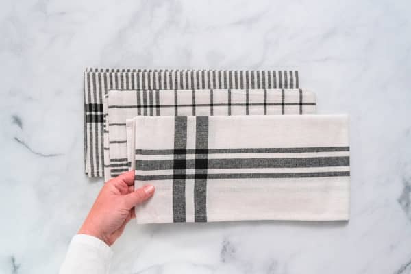 New kitchen towels with simple black pattern folded on marble counter.