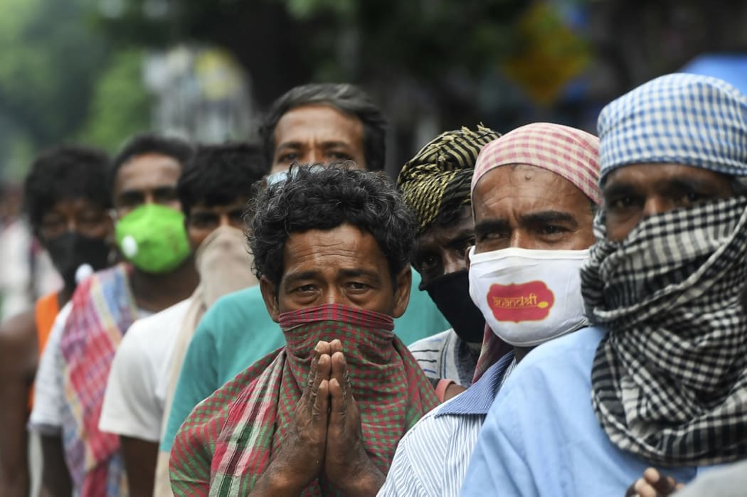 Homeless people wait in a queue to collect free food on the side of a road during a complete lockdown announced by the state government, in Kolkata on July 25, 2020.