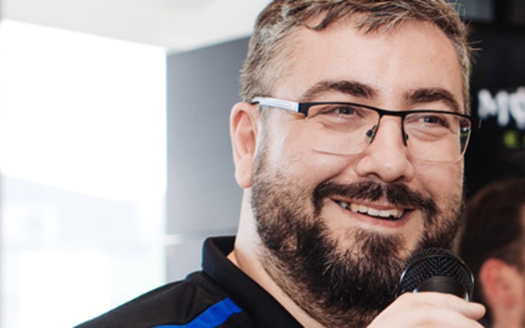 Photo of a man holding microphone and speaking in a pleasant manner.