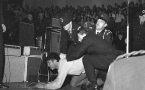 The second Beatles' concert at the Wellington Town Hall on 23 June 1964. Two policemen and a security guard are restraining a fan near the stage. from The Dominion Post Collection, Alexander Turnbull Library