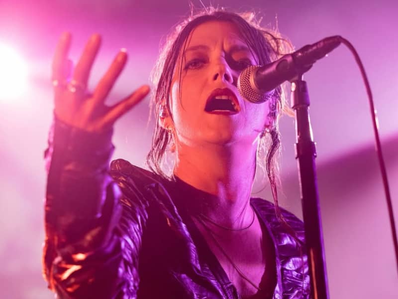 Sharon Van Etten sings into a microphone with one hand raised.