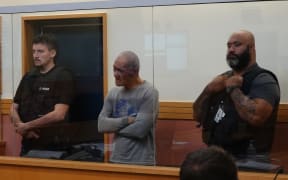 Abel Wira, who is accused of owning the dogs that mauled Neville Thomson in Panguru last year, is flanked by security guards in the Kaitāia District Court. Photo: RNZ / Peter de Graaf