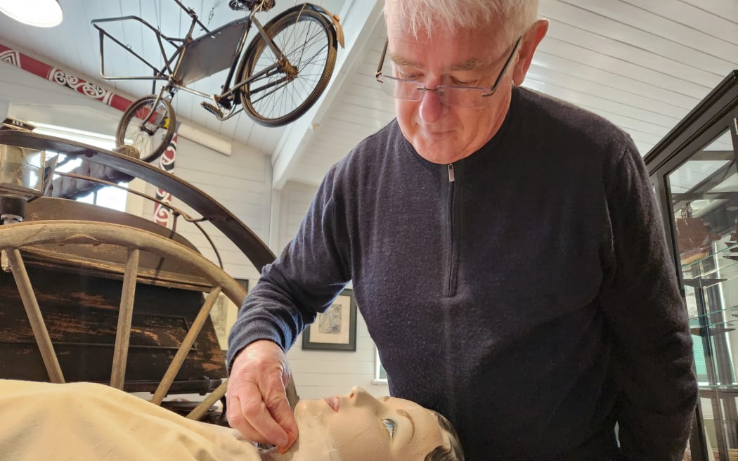 Chris Petersen bent over a mannequin. He is touching up her damaged face getting her ready for display