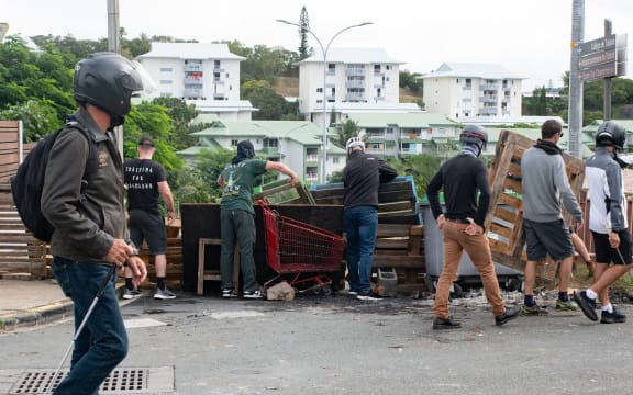 Masked residents of neighborhoods south of the capital, set-up roadblocks to block access and channel pro-independence activists at the entrance to Tuband, in the Motor Pool district of Noumea on May 15, 2024, amid protests linked to a debate on a constitutional bill aimed at enlarging the electorate for upcoming elections of the overseas French territory of New Caledonia. One person was killed, hundreds more were injured, shops were looted and public buildings torched during a second night of rioting in New Caledonia, authorities said Wednesday, as anger over constitutional reforms from Paris boiled over. (Photo by Delphine Mayeur / AFP)