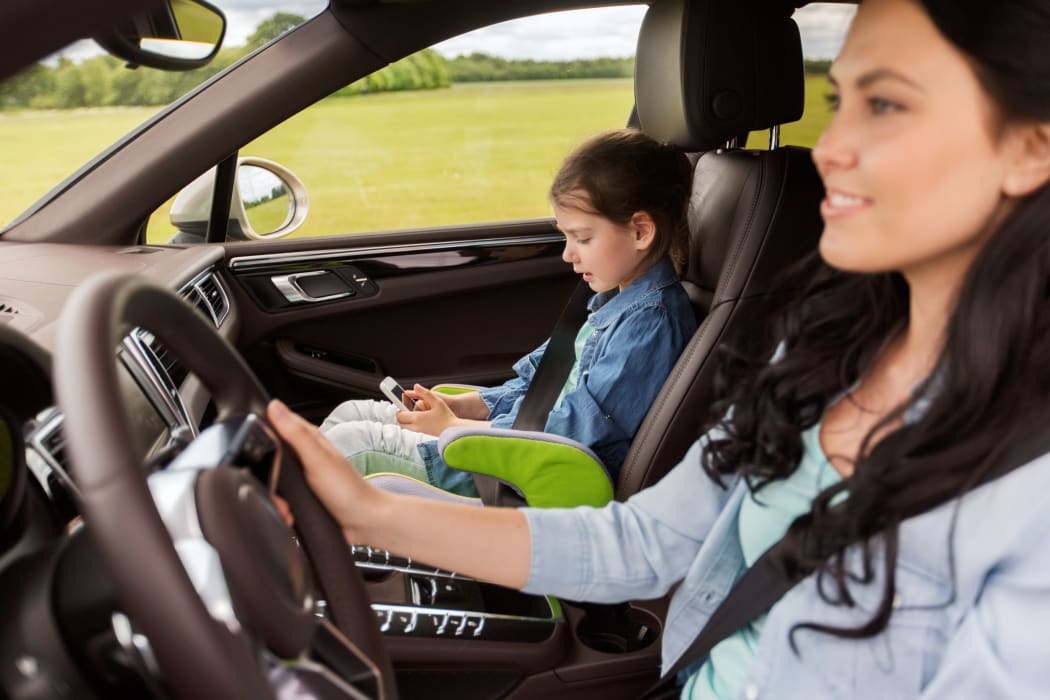 A photo of a mother driving in the car with her daughter who is looking at a  smartphone