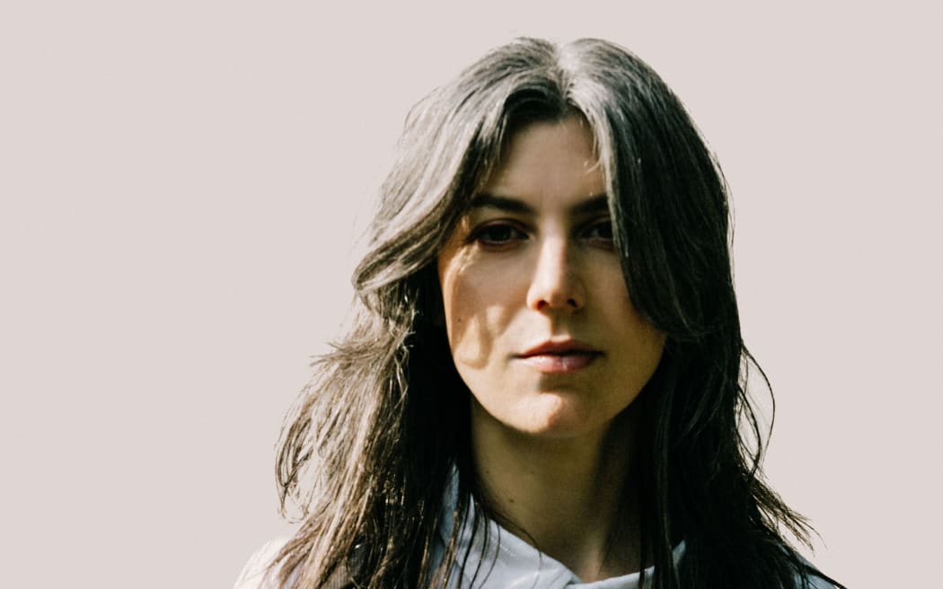 Singer and composer Julia Holter standing face to the camera in a white shirt and tie undone.
