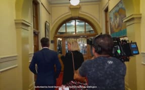 Mihingarangi Forbes follows David Seymour down a corridor in Parliament in an attempt to interview him. Following them is a cameraman.