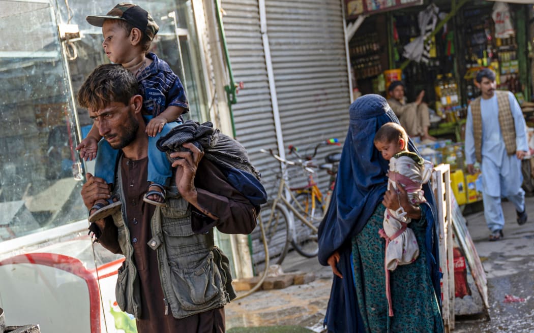 An Afghan man and burqa-clad woman carry their children as they walk past a market near the Pul-e Khishti mosque in Kabul on 20 July 2022.