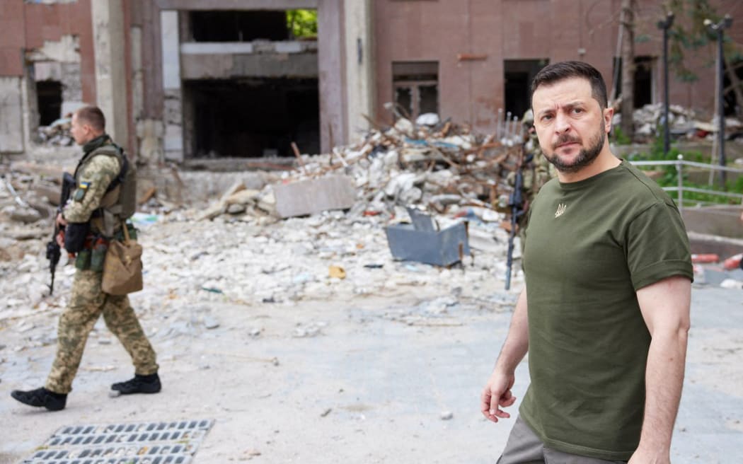 This handout picture taken and released by the press service of the Ukrainian Presidency on 18 June, 2022 shows Ukrainian President Volodymyr Zelensky (R) walking past a partially destroyed building during his visit to the position of Ukrainian troops in Mykolaiv region. (Photo by Handout / UKRAINE PRESIDENCY / AFP) / RESTRICTED TO EDITORIAL USE - MANDATORY CREDIT "AFP PHOTO/ PRESS SERVICE OF THE UKRAINIAN PRESIDENCY" - NO MARKETING - NO ADVERTISING CAMPAIGNS - DISTRIBUTED AS A SERVICE TO CLIENTS