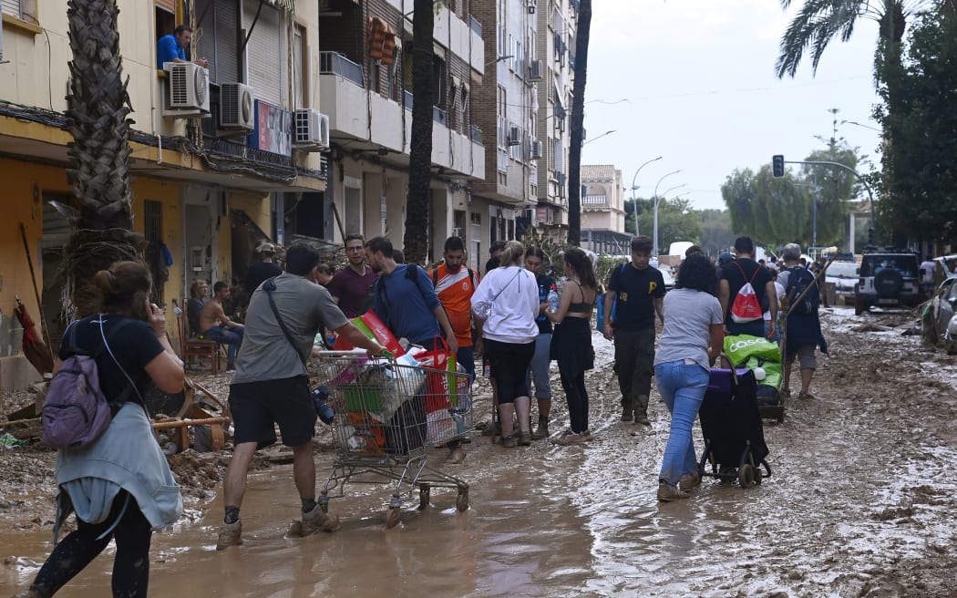 People push shopping carts along a street covered in mud on October 31, 2024 after flash floods ravaged Paiporta, in Valencia, eastern Spain. - Rescuers raced on October 31, 2024 to find survivors and victims of once-in-a-generation floods in Spain that killed at least 95 people and left towns submerged in a muddy deluge with overturned cars scattered in the streets. About 1,000 troops joined police and firefighters in the grim search for bodies in the Valencia region as Spain started three days of mourning. Up to a year's rain fell in a few hours on the eastern city of Valencia and surrounding region on October 29 sending torrents of water and mud through towns and cities. (Photo by JOSE JORDAN / AFP)