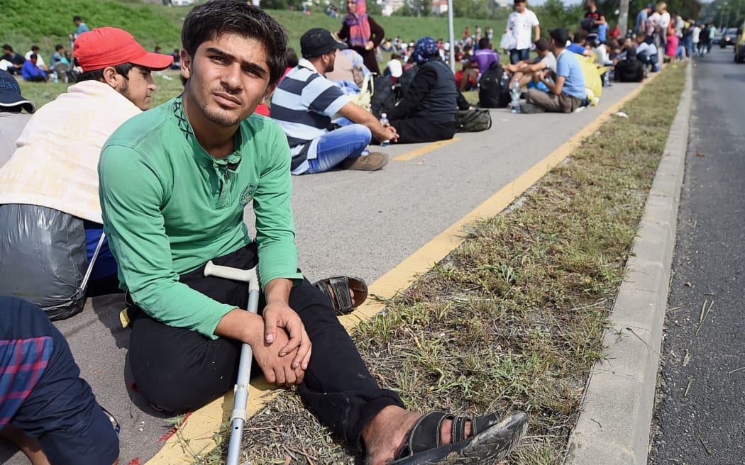 A migrant group of about 500 refugees sits on the pavment next to the main road near Budaors, Hungary, as they head to the Hungarian-Austrian border.