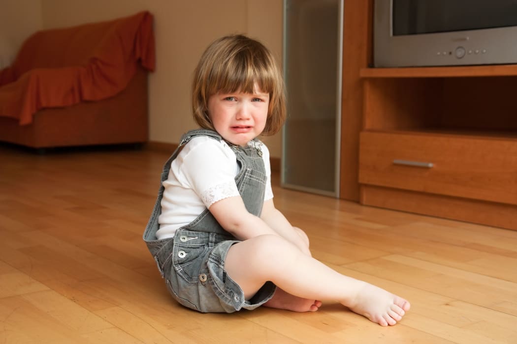 A photo of a crying girl sittng on a  wooden floor