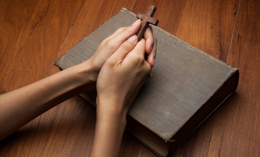 Hands folded in prayer over Holy Bible