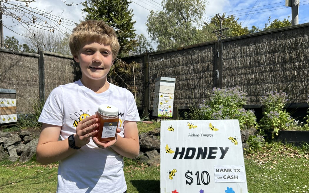 Picture depicts a child beekeeper, holding a small jar of honey.