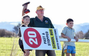 Outram School bus driver Ken Schumacher, flanked by brothers Walter, 8 (left), and George Morrisey, 5, holds a sign designed to get speeding motorists to slow down. PHOTO: PETER MCINTOSH/ODT