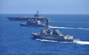 Three US Navy ships, lead by the aircraft carrier USS Nimitz, operate in formation in the South China Sea.
