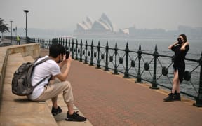 Tourists wearing masks take photos as the Opera House (back, C) is enveloped in haze caused by nearby bushfires, in Sydney on December 10, 2019.