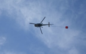 A helicopter with a monsoon bucket fights a fire at Arthur's Pass.