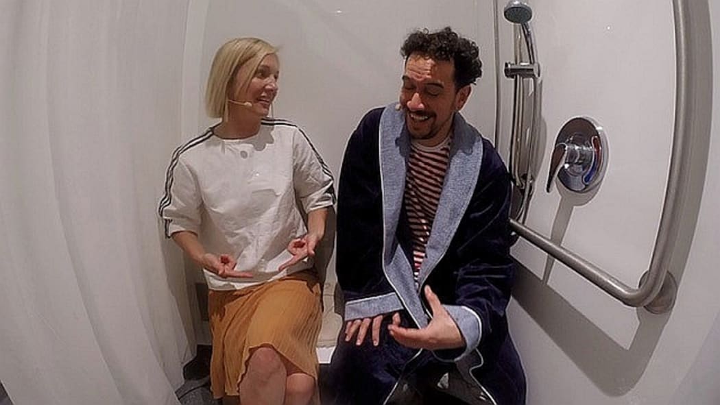 Hayley Holt and James Nokise sitting side by side in a shower and laughing.