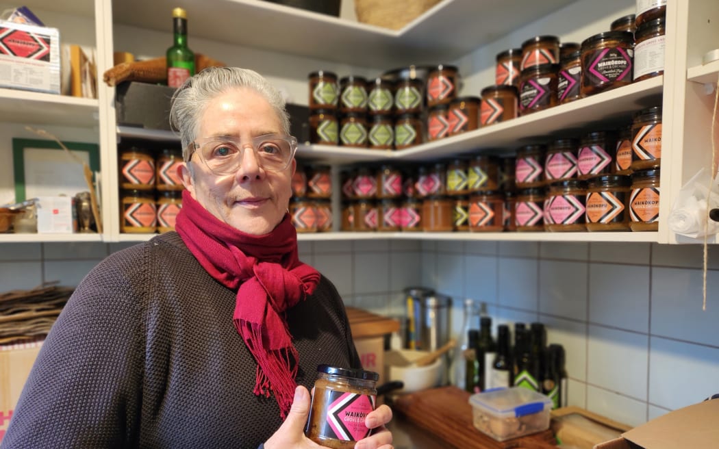 Huhana Smith holding a jar of preserves in front of shelves of preserves stacked in rows