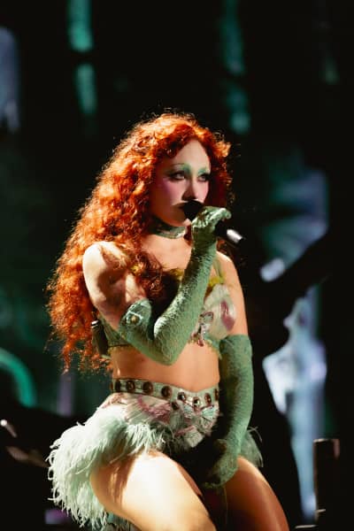 Chappell Roan, wearing green gloves and a green choker, sings into a microphone as lighting hits her red wavy hair.