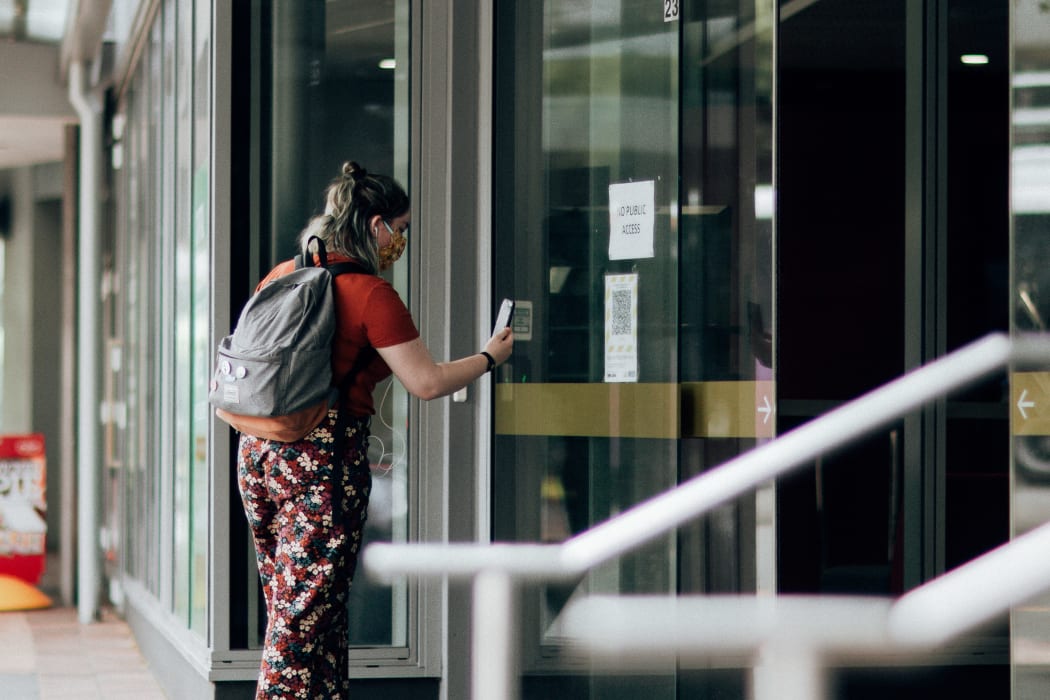 A woman using the Covid Tracer app at a QR code in the window of a business during level 2 in Wellington on15 February 2021