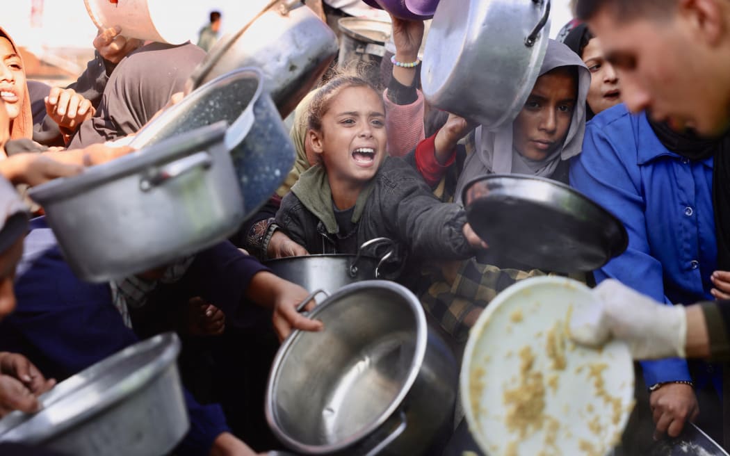 Displaced Palestinians gather to receive donated food portions at a charity kitchen in Khan Yunis.