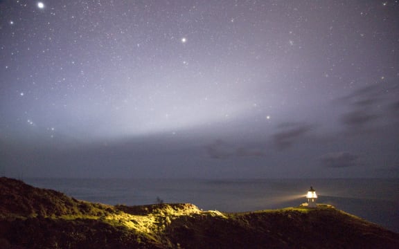 A serene night sky filled with stars above a lighthouse illuminating the coastline, Cape Reinga, New Zealand (Photo by Peter Evans / Connect Images via AFP)