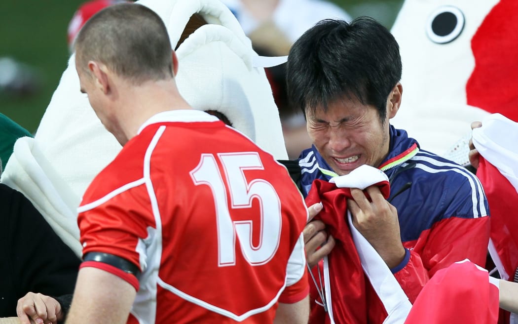 Japan's Shaun Webb walks past a dejected Japanese fan after losing to Canada.