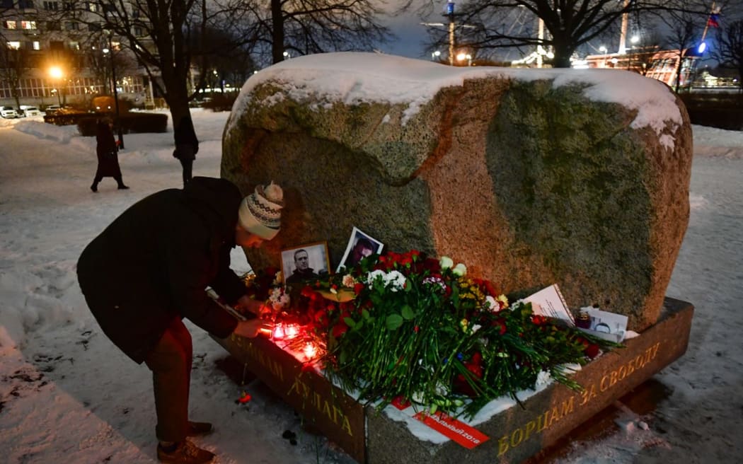 A man places a lit candle at a makeshift memorial for late Russian opposition leader Alexei Navalny organized at the monument to the victims of political repressions in Saint Petersburg on February 16, 2024, following Navalny's death in his Arctic prison. (Photo by Olga MALTSEVA / AFP)