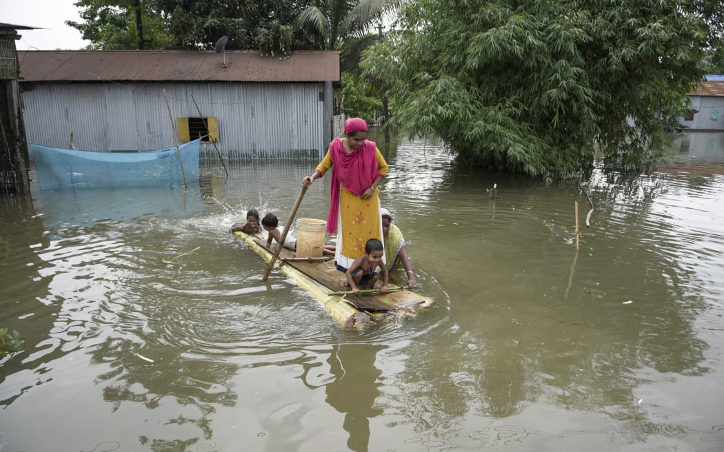 Woman with children moves on a banana raft in front of their flooded house, in a village in Barpeta, in India's northeastern state of Assam on 20 June, 2022.