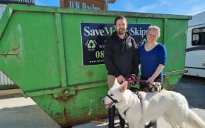 South Dunedin residents Gareth and Dyan O'Malley and their dogs Bolt and Blaze in front of a skip full of their flood-wrecked belongings.