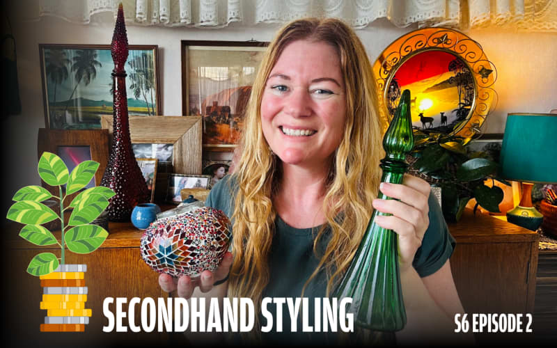A smiling woman with long, wavy blonde hair stands in a cozy, vintage-styled room, holding a green glass bottle in one hand and a colourful mosaic bowl in the other. Behind her is a wooden sideboard decorated with framed art, retro ornaments, tall decorative bottles, plants, and a sunset-themed lamp. Text on the image reads: “SECONDHAND STYLING – S6 EPISODE 2.”