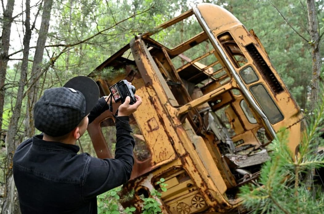 A visitor takes a picture at a wreckage of a bus in the ghost city of Pripyat during a tour in the Chernobyl exclusion zone on June 7, 2019.