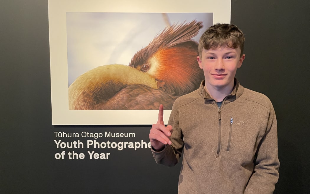 Monty McGee standing by his photo of a native crested grebe. The photo is called Pūteketeke Yoga.