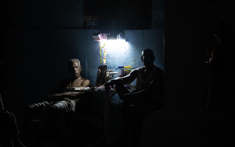 People sit around a table illuminated by a small light source during a nationwide blackout in Havana on July 6, 2026. Cuba on July 6 suffered its third nationwide power outage since the start of the year, the state electricity company said. The impoverished island was already struggling to keep the lights on before US President Donald Trump in January imposed an oil blockade, which has depleted the already dwindling supply of fuel for Cuba’s power plants. (Photo by YAMIL LAGE / AFP)