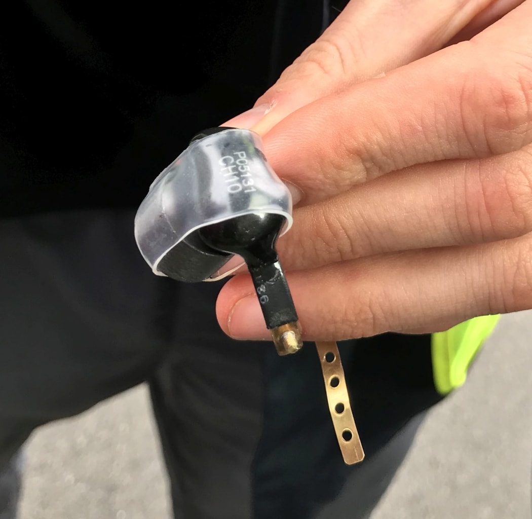 Radio tracking device for rats attached to a small collar. When it is in use, the plastic cover and the large magnet (left) are removed to activate the transmitter.