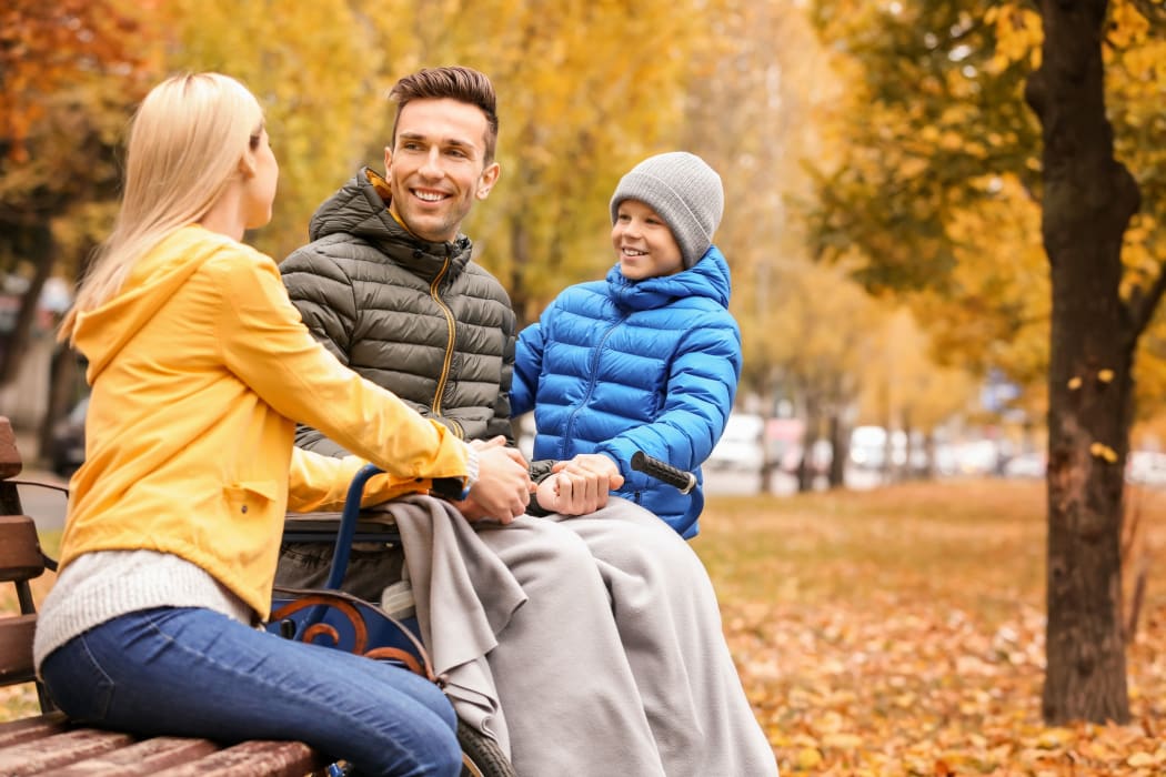 A photo of a Man in wheelchair with his family outdoors on autumn day