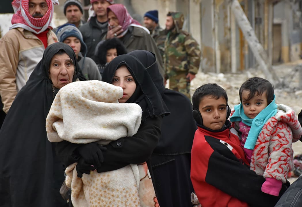 Syrian residents fleeing the eastern part of Aleppo walk through a street in Masaken Hanano, a former rebel-held district which was retaken by the regime forces last week, on November 30, 2016.